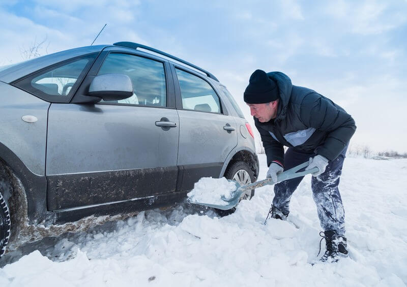 man shoveling snow off car